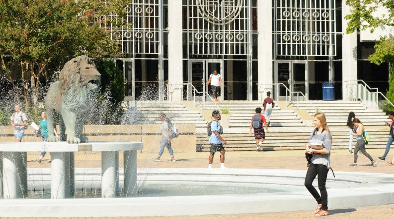 A group of students walk in front of the lion statue and fountain.