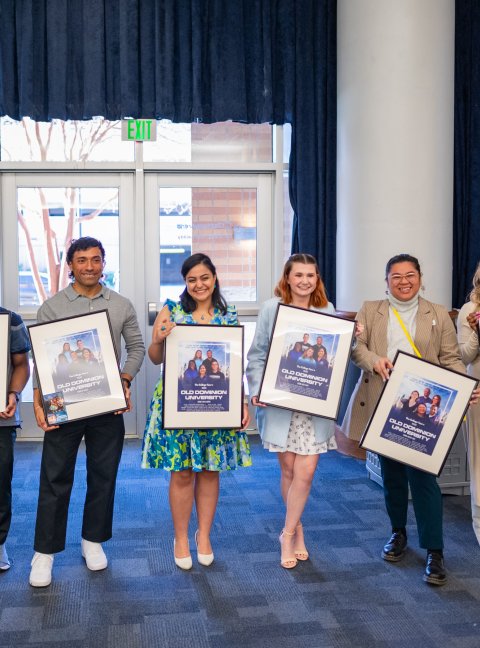 students standing while each holding a framed movie poster 