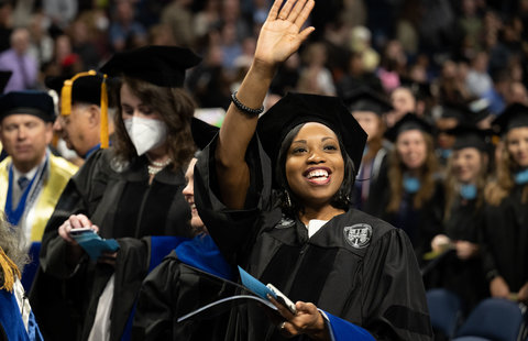 an odu doctoral student waves to the crowd with a diploma in her hand